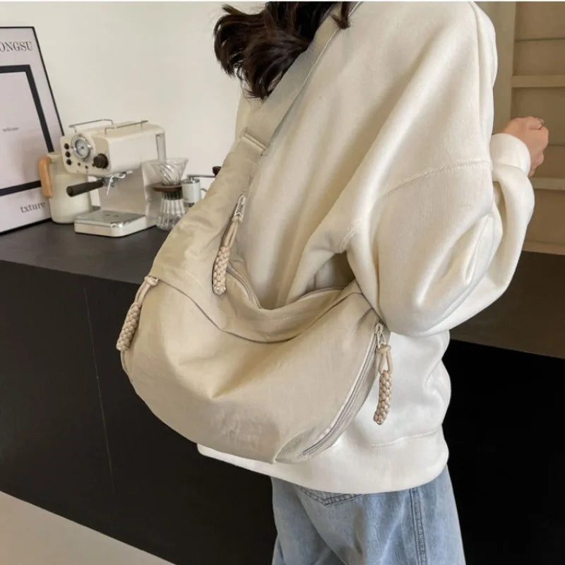 A person wearing a cream-colored hoodie carries a beige lightweight nylon crossbody bag.