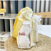 A yellow transparent shoulder bag with white fur trim and lace detailing resting on a woven mat.