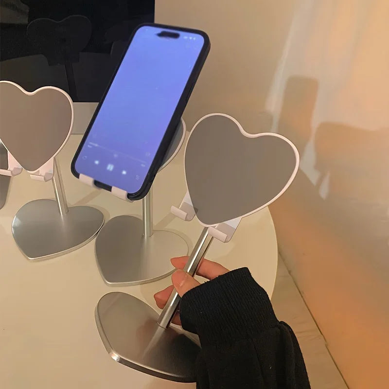 A hand is adjusting an adjustable heart-shaped stand designed to hold a smartphone or tablet.
