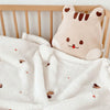 A soft, cream-colored coral fleece baby blanket with bear embroidery draped over a wooden crib rail.