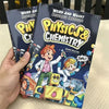 A hand holds a set of two physics and chemistry comic books featuring characters in lab coats and space gear.