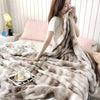 A woman is relaxing on a bed covered with a fluffy gradient beige fleece throw blanket.