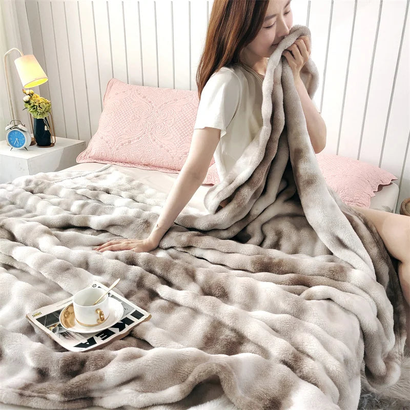 A woman is relaxing on a bed covered with a fluffy gradient beige fleece throw blanket.