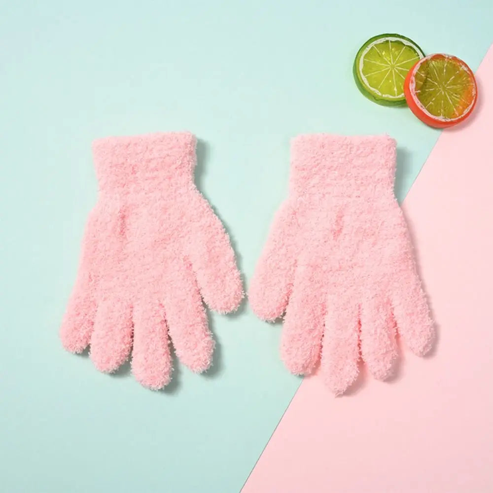 Pair of pink fuzzy plush winter gloves resting on a light blue background next to a lime and orange slice.