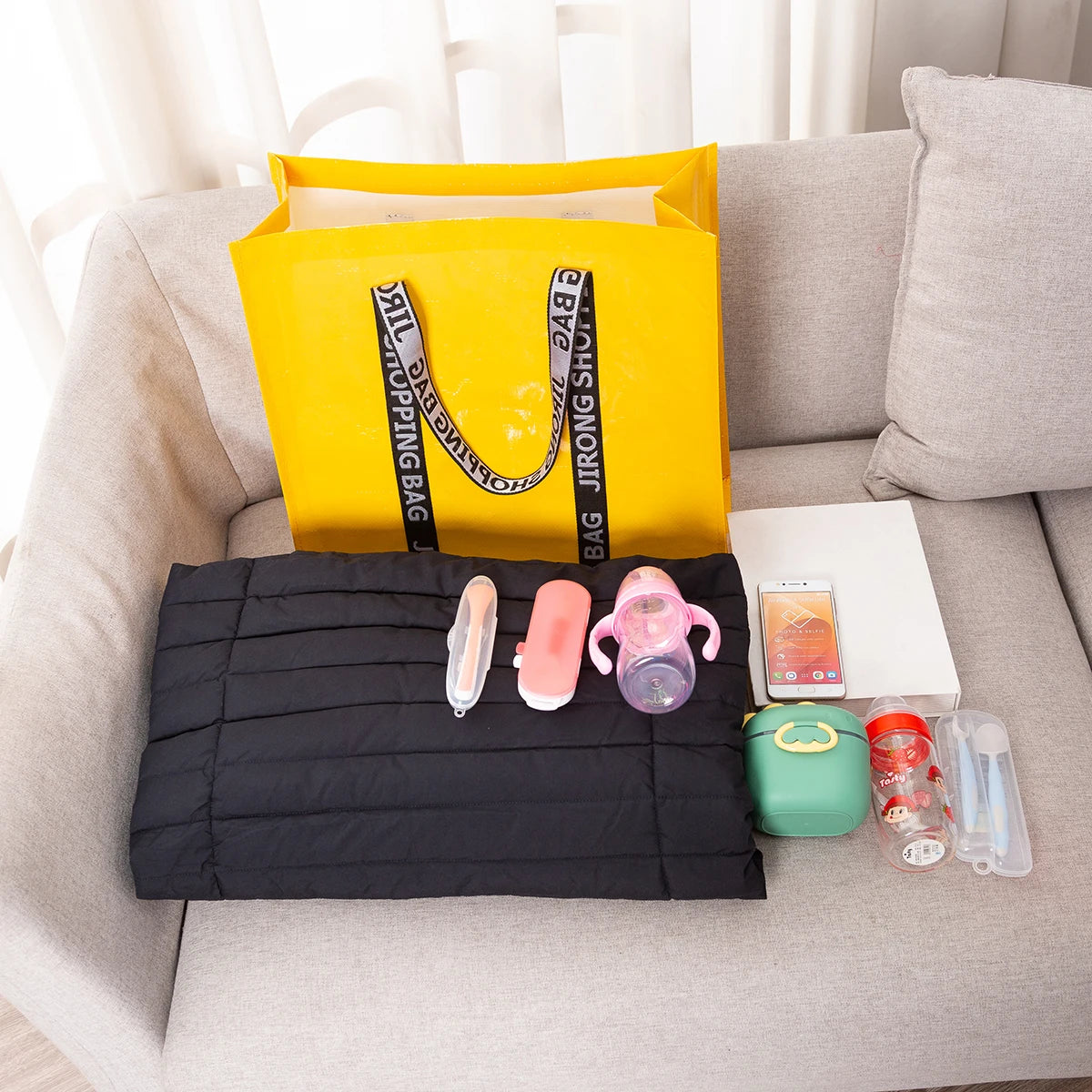A yellow tote bag with black straps is displayed on a light gray sofa next to various personal items.