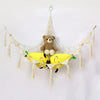 A bohemian plush toy storage hammock made of macrame netting with hanging tassels, holding a brown teddy bear and two yellow 