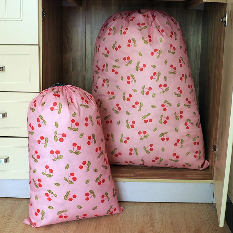 A pink drawstring laundry bag with a red cherry pattern is displayed on a wooden shelf.