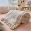 A rolled floral washed cotton gauze summer quilt with delicate lace trim resting on a pink surface.