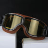 A pair of brown retro foldable motorcycle goggles with gold tinted lenses resting on a white box.