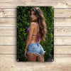 A young woman with long brown hair wearing a purple top and distressed denim shorts posing outdoors.