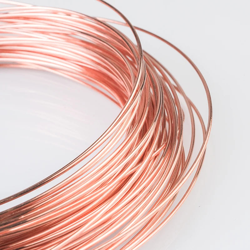 A coil of reddish-copper wire with multiple diameters laid out on a white surface.