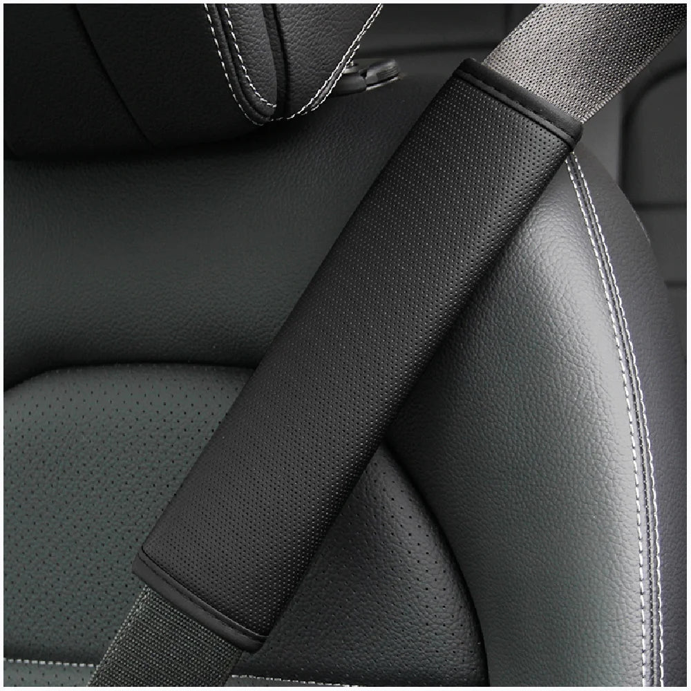 A close-up of a black PU leather embossed seat belt shoulder cushion on a dark car seat.