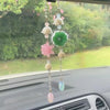 A pink lotus car pendant featuring multiple dangling beads and a green feather charm displayed on a car interior.