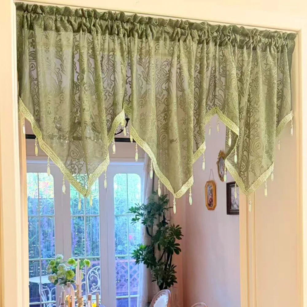 A sheer sage green lace curtain valance with irregular black window pendants hangs over a light-colored door frame.