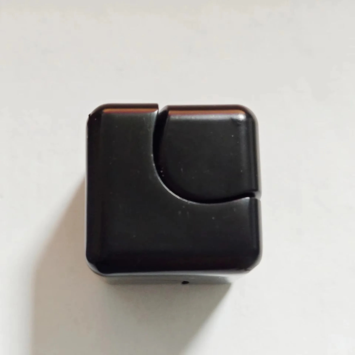 A black metal fidget spinner cube with a curved design.