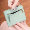 A hand is holding a light mint green bi-fold wallet with a zippered compartment and an RFID protection shield.
