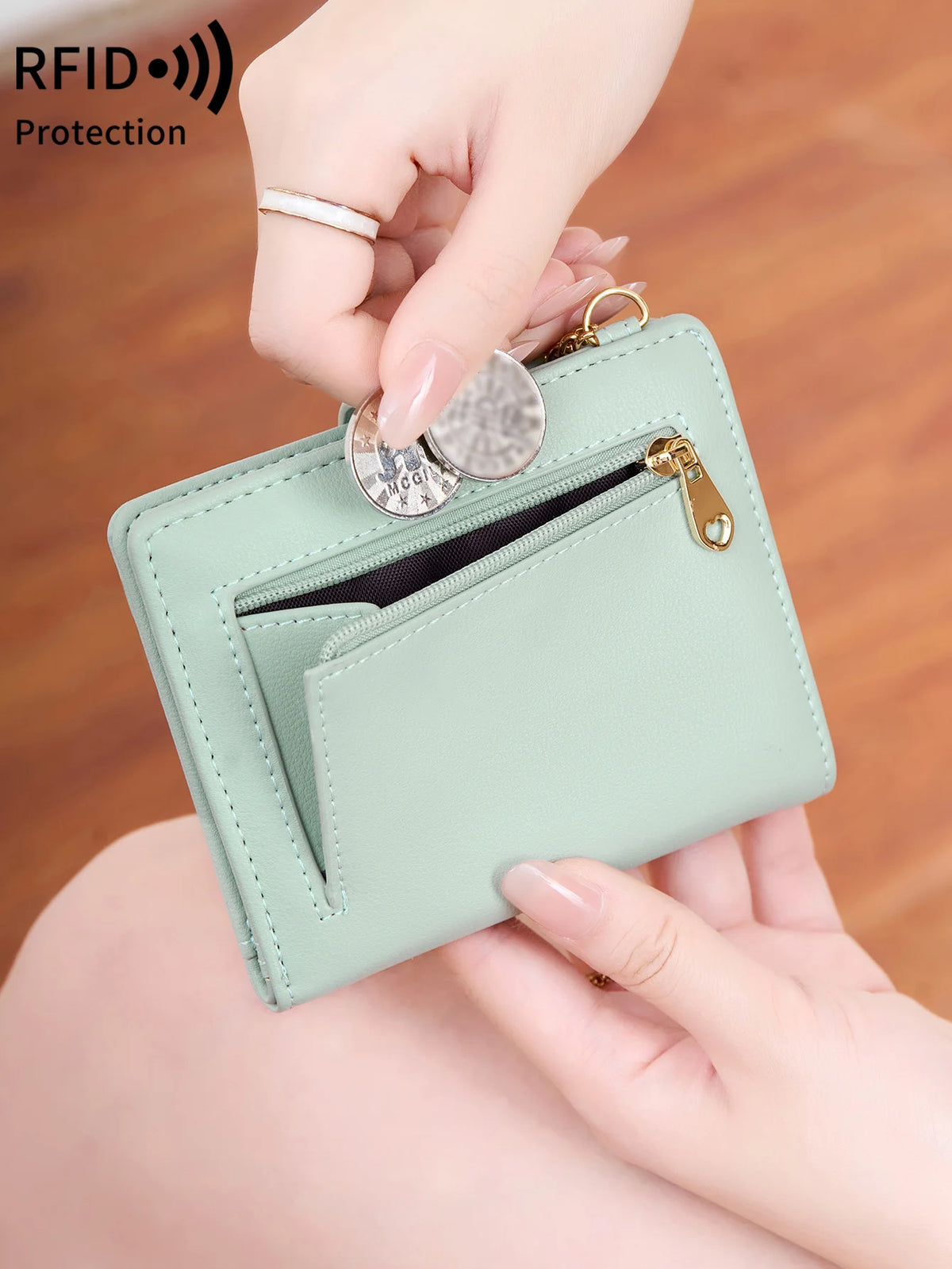 A hand is holding a light mint green bi-fold wallet with a zippered compartment and an RFID protection shield.