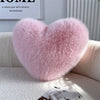 A fluffy pink heart-shaped throw pillow resting on a white sofa.