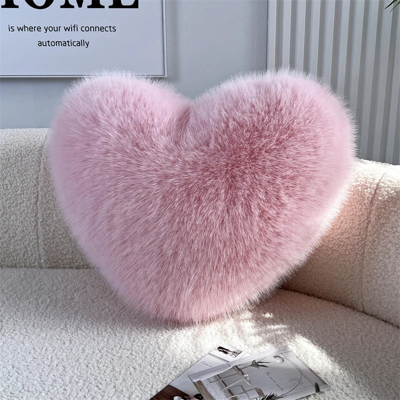 A fluffy pink heart-shaped throw pillow resting on a white sofa.