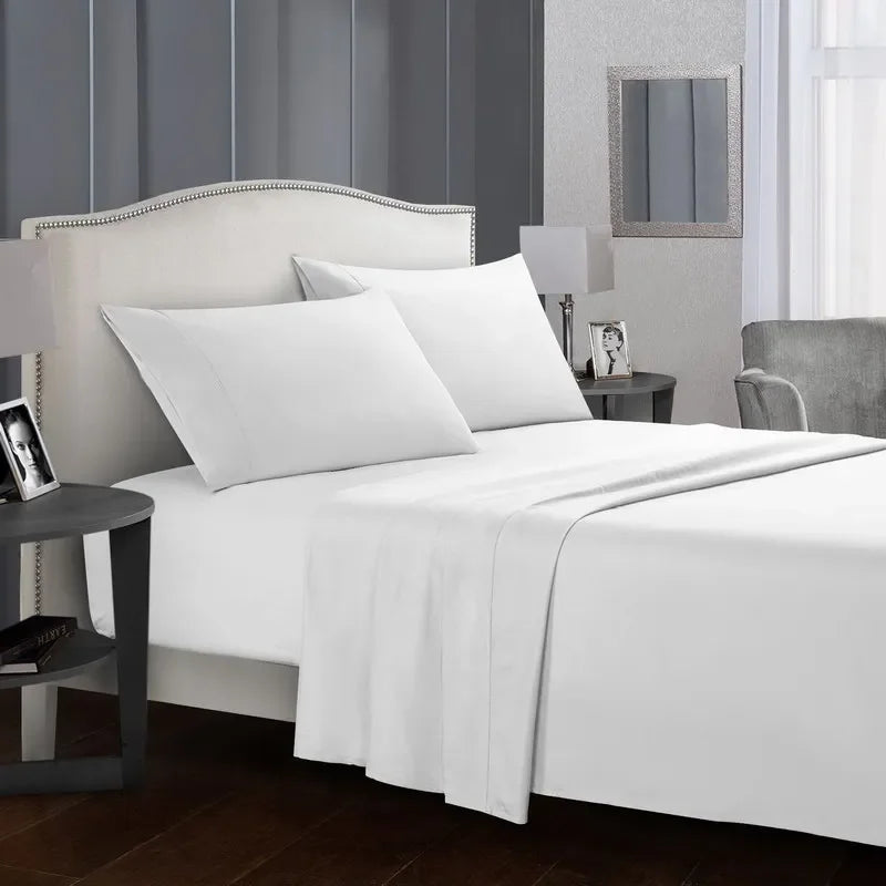A white bed with a headboard and bedding set featuring white sheets, pillows, and a white duvet in a modern bedroom.