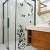 A modern bathroom vanity featuring a white countertop and wooden cabinet with black flower butterfly wall stickers on the gla