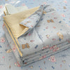 A stack of light gray and beige cartoon pattern kids lightweight summer quilts on a blue quilted surface.