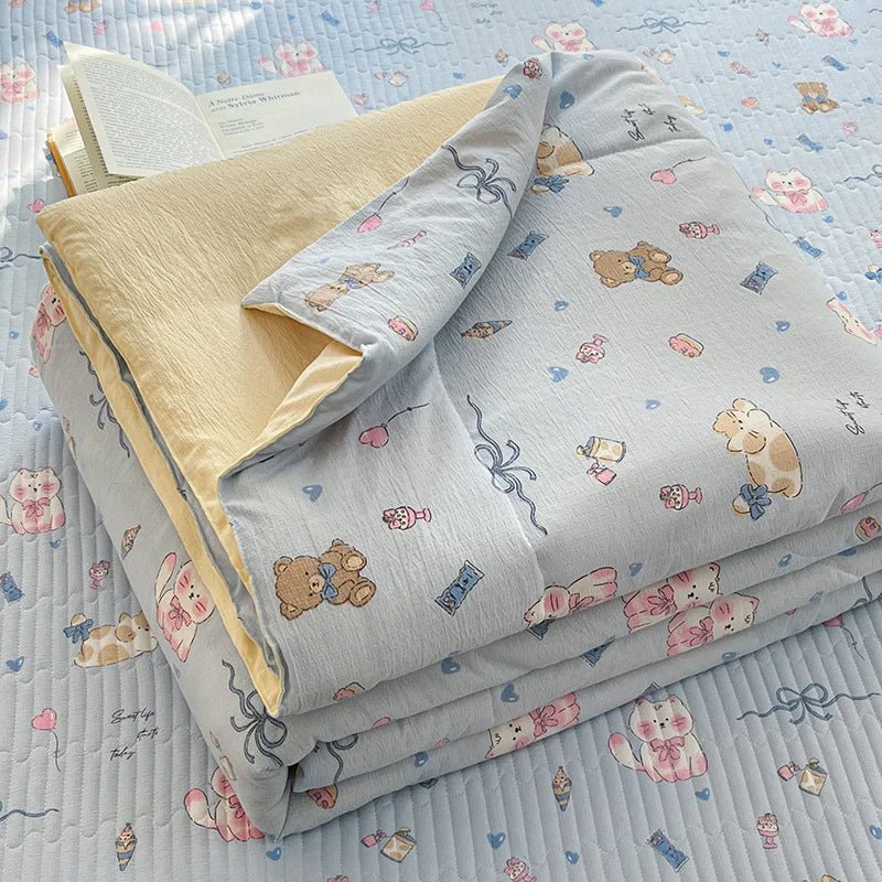 A stack of light gray and beige cartoon pattern kids lightweight summer quilts on a blue quilted surface.