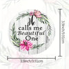 A circular wooden coaster featuring a wreath of green leaves and pink flowers with the text He calls me Beautiful One.