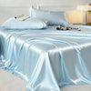 Light blue satin bed sheets draped elegantly on a bed with white bedding and a lamp.
