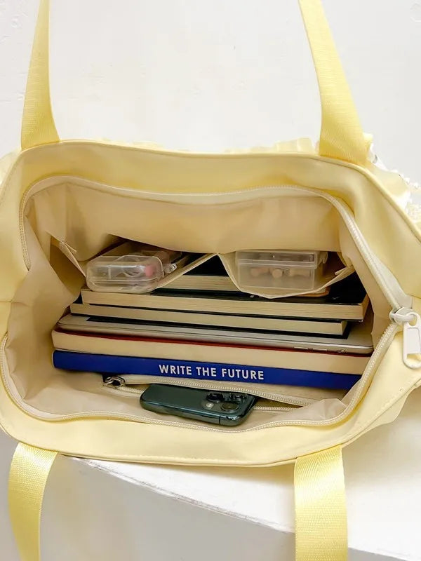 A pale yellow shoulder bag with a lace trim, featuring a clear pocket holding books and a smartphone.