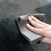 A hand is wiping a dark surface with a gray microfiber cleaning cloth.