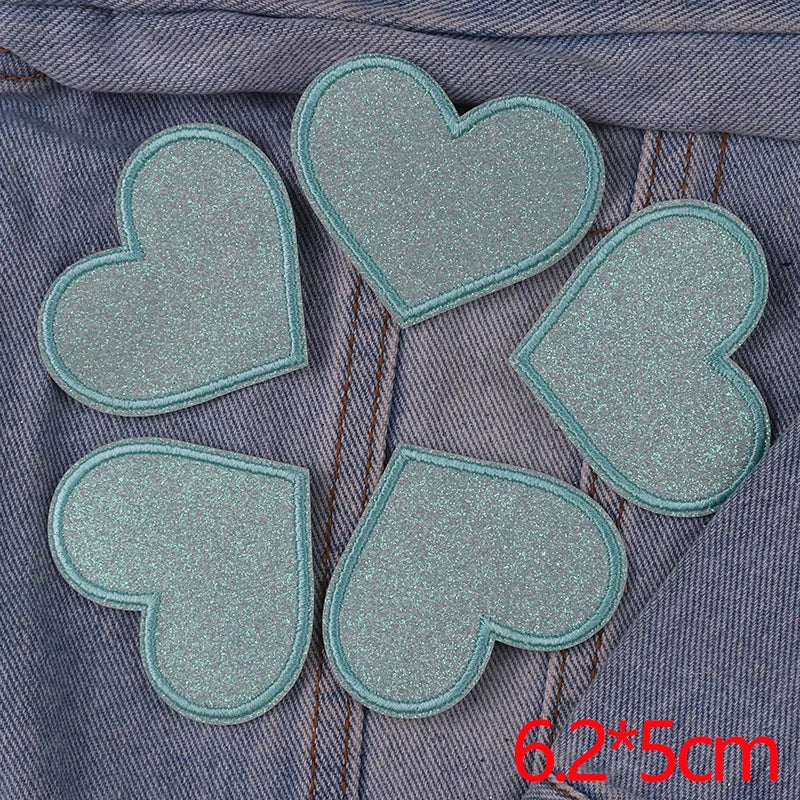 A set of five light blue glitter heart iron-on embroidered patches laid out on a denim fabric background.