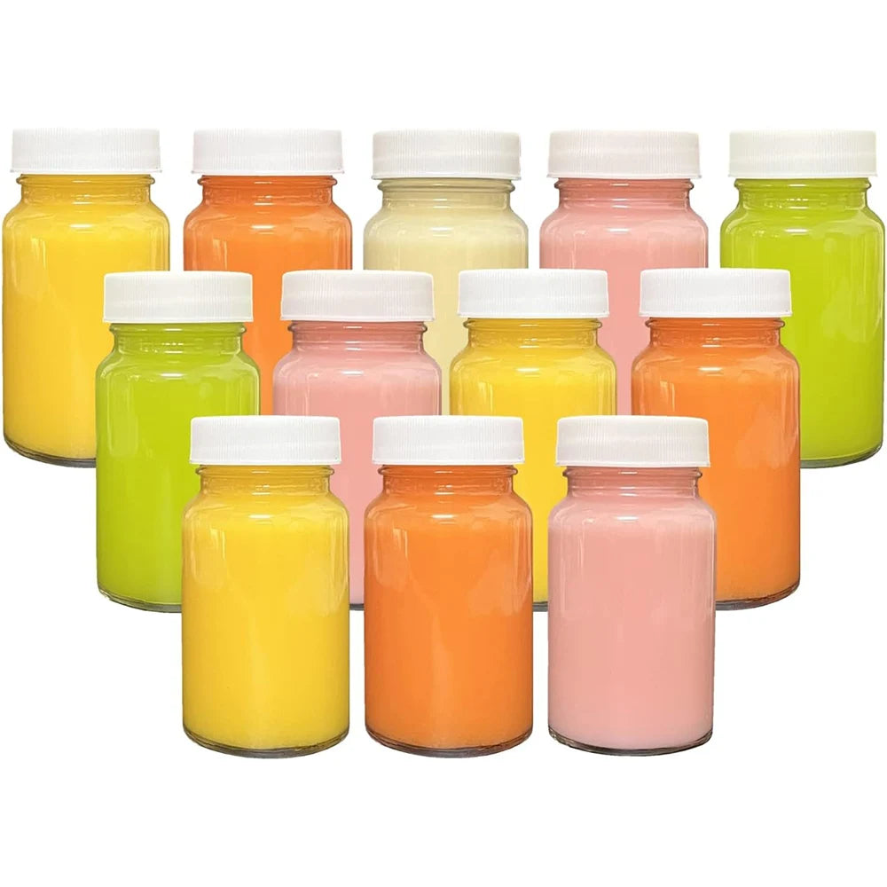A collection of twelve 2oz glass juice bottles filled with various fruit juices in shades of yellow, orange, pink, and green.