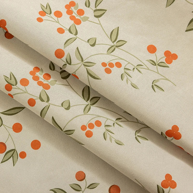 A close-up of a beige curtain panel fabric featuring an orange and green plant pattern.