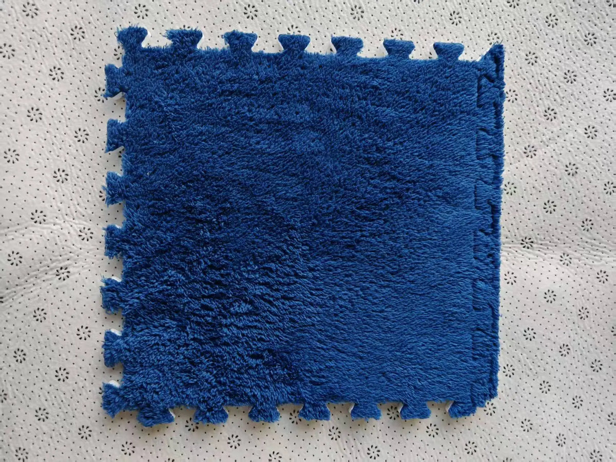A rectangular blue plush interlocking floor tile resting on a light-colored, perforated surface.