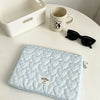 A light blue quilted laptop sleeve with a soft lining resting on a white table next to a mug and sunglasses.
