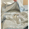 A light blue and white striped breathable summer quilt draped over a bed, with a small wooden item resting on top.