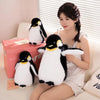 A young woman is sitting on a couch with two black and white penguin plush toys.