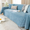 A light blue waterproof anti-slip sofa cover draped over a sofa with decorative pillows and a book.