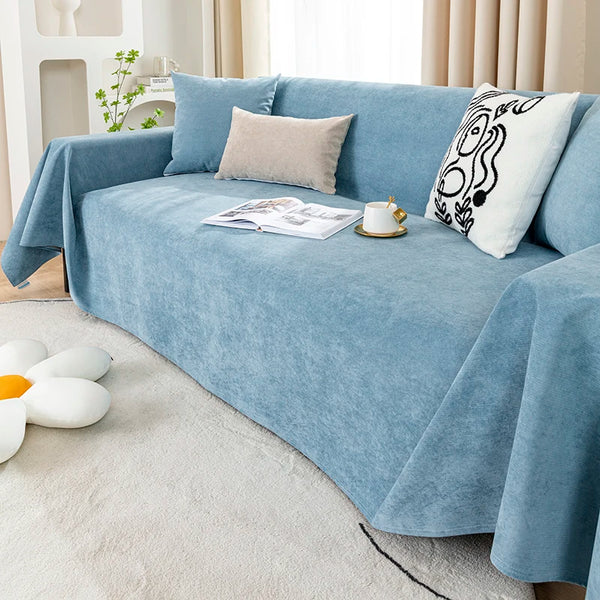 A light blue waterproof anti-slip sofa cover draped over a sofa with decorative pillows and a book.