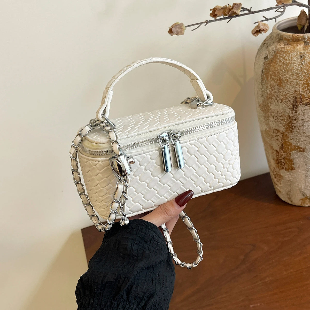 A white quilted woven PU leather crossbody bag with silver chain details is held by a hand against a light background.