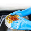 A hand wearing blue scrubber-textured dishwashing gloves is washing a plate with orange-colored food residue.
