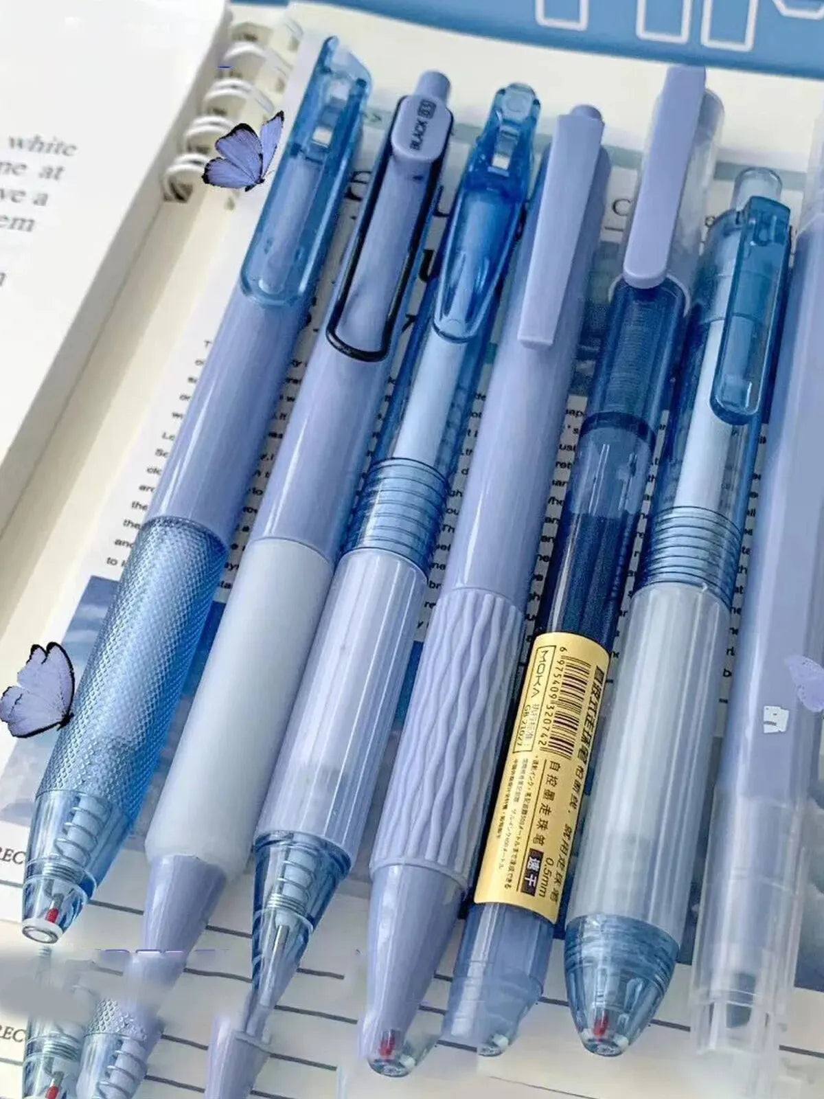 A pack of seven minimalist clear gel pens in various shades of blue and purple are displayed in a clear plastic case.