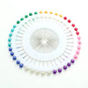 A circular arrangement of colorful round pearl straight pins in various shades of green, yellow, and red.