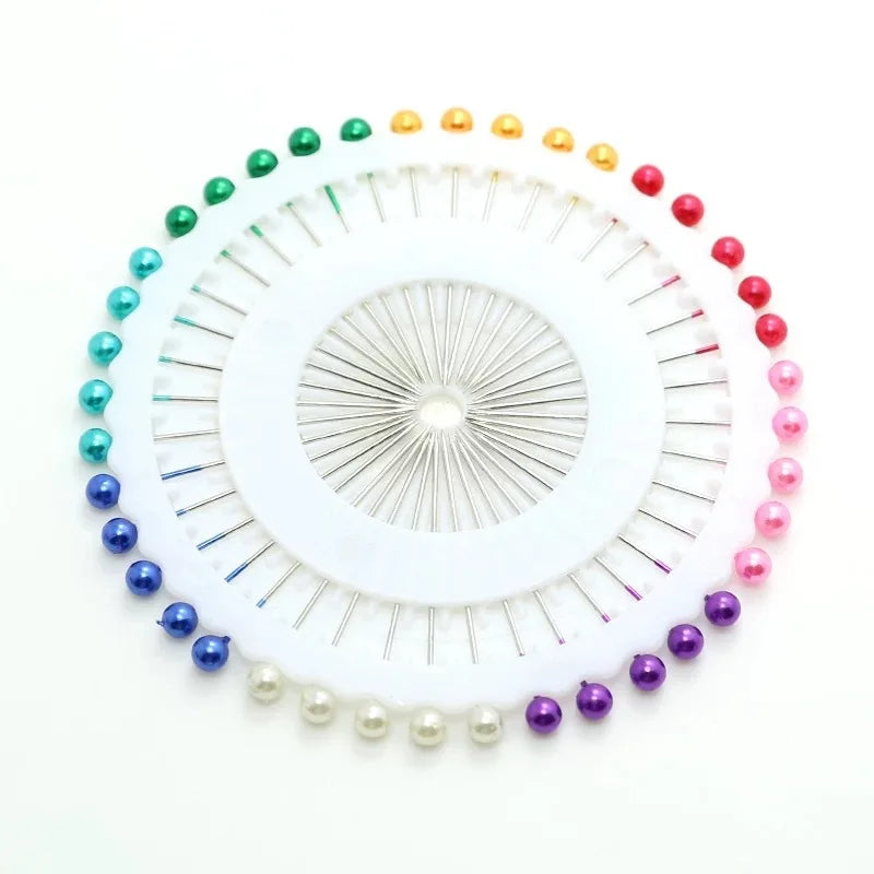 A circular arrangement of colorful round pearl straight pins in various shades of green, yellow, and red.