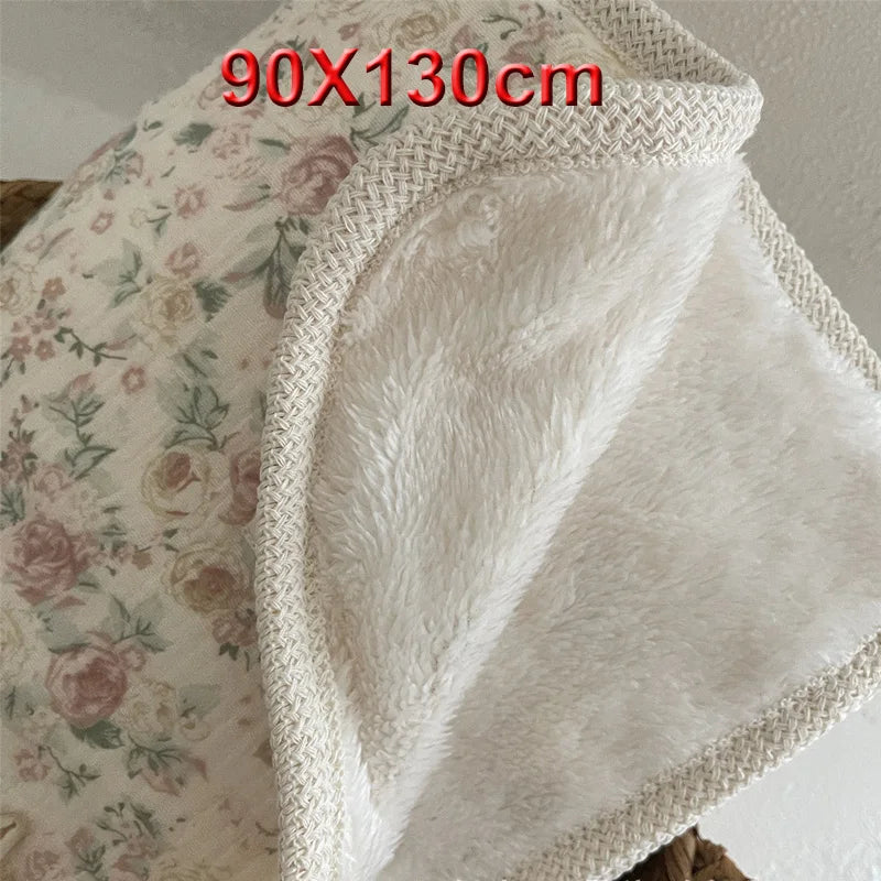 A white floral muslin baby blanket with a textured, fluffy trim is shown folded.