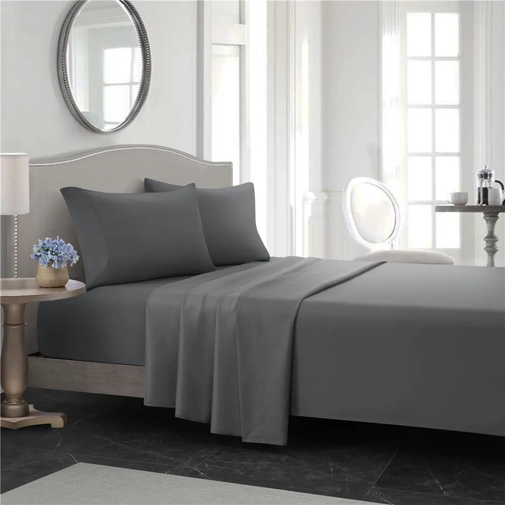 A gray bedding set featuring a fitted sheet, flat sheet, and pillowcases on a bed in a bright room.