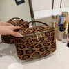 A brown leopard print cosmetic bag with a zipper is displayed on a white surface.