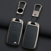 A pair of metallic car key case covers with attached split rings resting on a dark surface.