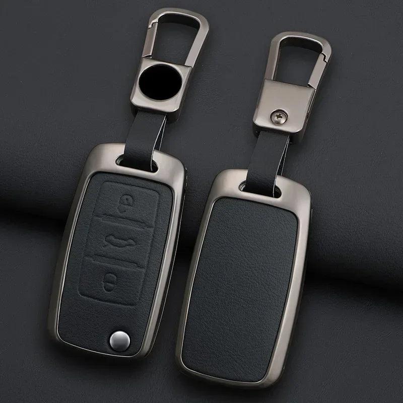 A pair of metallic car key case covers with attached split rings resting on a dark surface.